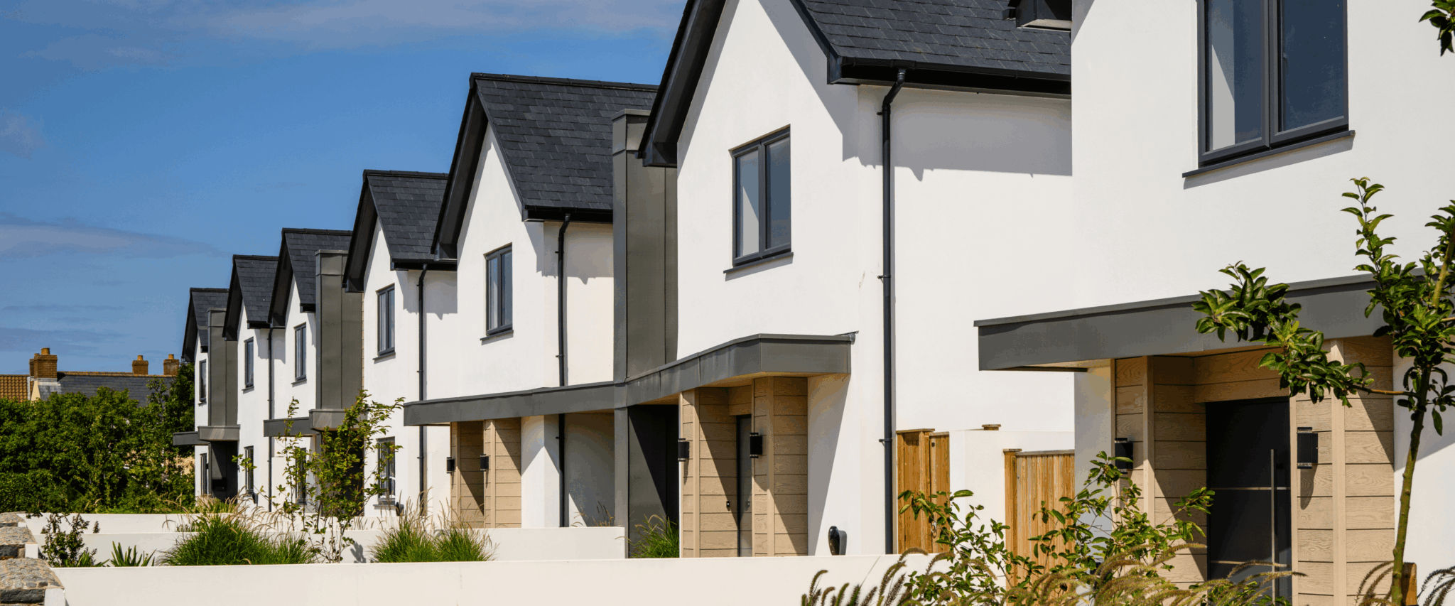 Row of new-build homes with grey windows and doors, finished in white render