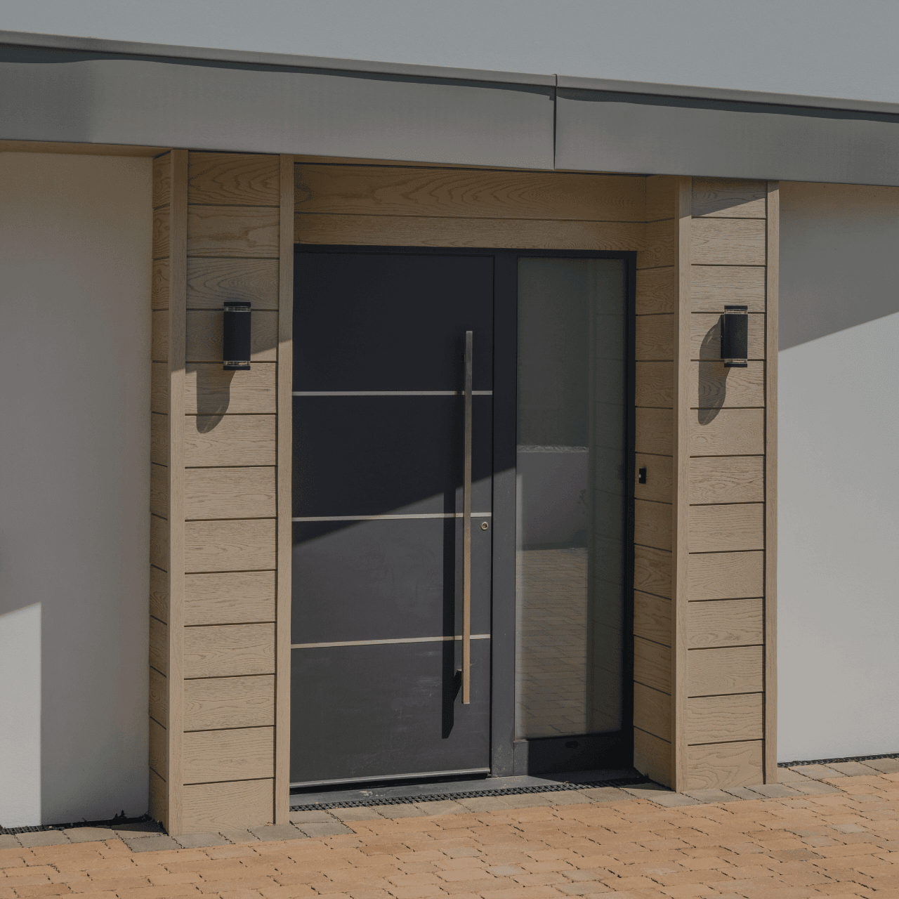 Grey aluminium front door with a long bar handle and timber cladding